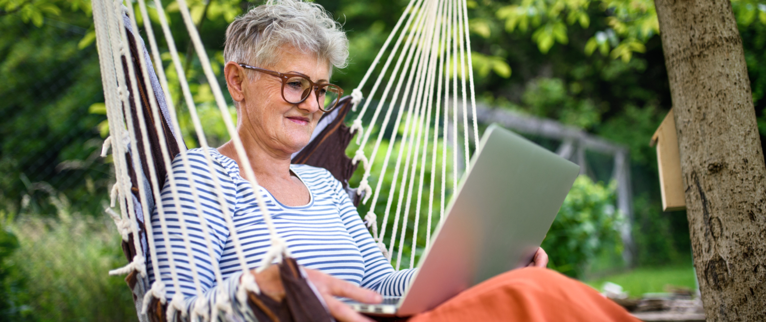 Portrait of active senior woman with laptop working outdoors in garden, home office concept.